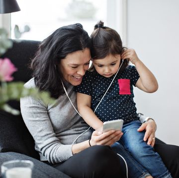 mother and daughter wearing headphones while listening music through mobile phone in living room